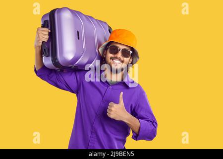 Felice uomo indiano che va in vacanza viaggio, portando valigia, sorridendo e dando i pollici in su Foto Stock