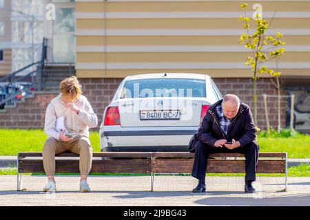 Minsk, Bielorussia - 18 maggio 2022: Persone e telefoni cellulari. Un giovane e un anziano che si fermano ai mezzi di trasporto pubblico guardano gli schermi dei loro dispositivi mobili Foto Stock