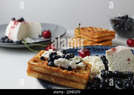 deliziosa colazione sana. Le cialde belghe morbide con crema di formaggio di curd e ciliegie di mirtillo si trovano in bianco blu vista piatto dalla parte superiore. Delizioso stile Foto Stock