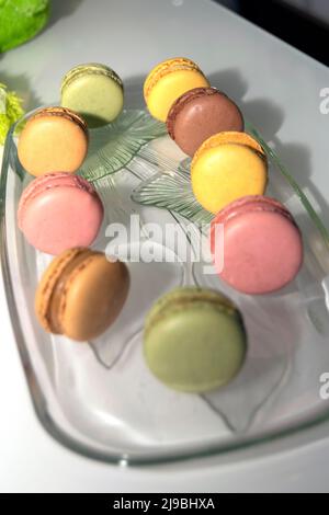 Macaron francesi colorati, biscotti con colori e sapori diversi su un piatto trasparente di vetro. Progettazione di alimenti. Foto Stock