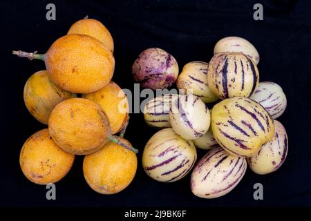Ecuador, Quito, Otavalo, mercato agricolo. granadilla dolce (Passiflora ligularis) (L) frutto della passione tropicale. Pepino dulce 'cetriolo di zeppa' (R). Foto Stock