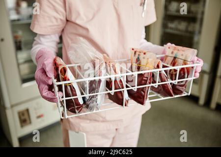 Primo piano di un vassoio di contenimento per infermiere non riconoscibile con sacche di sangue nel centro di donazione o in clinica, spazio copia Foto Stock