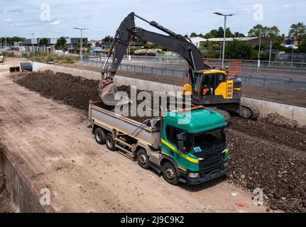 Una macchina scavatrice per impianti pesanti che carica un autocarro ribaltabile con olio proveniente da un'unità di ingegneria ferroviaria Foto Stock