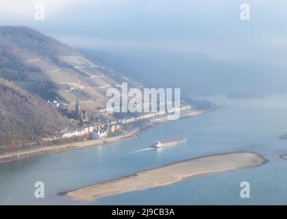 Nave accanto a un bar di sabbia nel fiume Reno vicino a Lorchhausen con la chiesa parrocchiale di San Bonifatio in una giornata di nebbia in Germania. Foto Stock