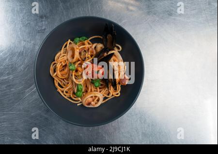 Pasta di pesce con cozze con basilico e pomodoro in piatto nero Foto Stock