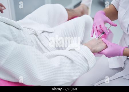 Medico cosmetologo che dà ringiovanimento iniezioni nel braccio del cliente uomo Foto Stock