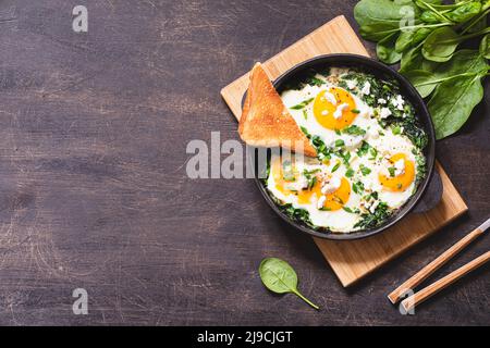 shakshuka verde in una padella in ghisa, uova fritte con spinaci e toast fritto. sana colazione nutriente, Foto Stock