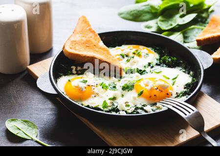 shakshuka verde in una padella in ghisa, uova fritte con spinaci e toast fritto. sana colazione nutriente, Foto Stock