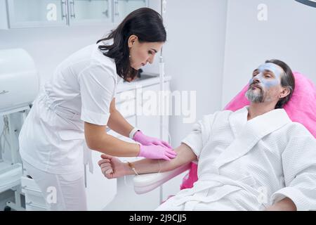 Cliente maschio bearded che riposa ed ottiene un'infusione endovenosa al salone di centro termale Foto Stock