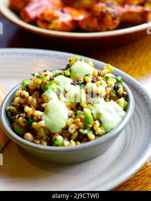 insalata di superfood sana con proteine ricche tra cui quinoa, avocado, fagioli e cereali. Ali di pollo sfocate sullo sfondo. Foto Stock