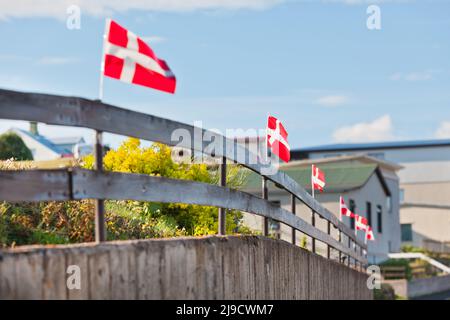 Bandiere bianche su rosse danesi in fila su una recinzione di legno in un villaggio scandinavo durante le festività nazionali Foto Stock