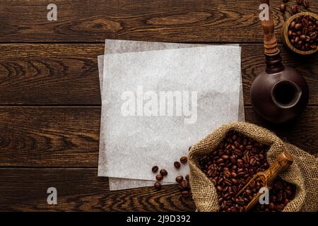 Chicchi di caffè appena tostati. Fondo in legno con accessori per la preparazione di bevande aromatiche calde e fogli di carta da imballaggio. Pentola cezve turca, woo Foto Stock