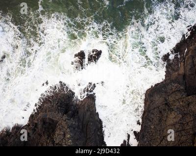 Vista dall'alto. Tempesta nell'oceano. Le onde bianche schiumose si infrangono contro grandi massi sulla riva. La grandezza e la bellezza della natura, l'ecologia, l'ambiente Foto Stock