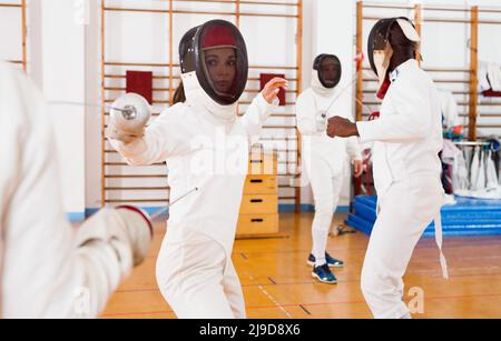 Due allegre fencer femmina sorridenti che esercitano i movimenti in duello nella stanza di scherma Foto Stock