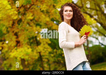 Bella giovane donna snella con capelli ricci lunghi cammina nella caduta nel parco e raccoglie le foglie Foto Stock