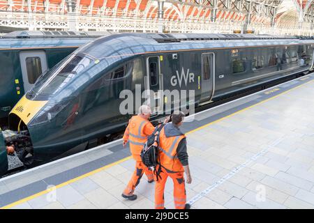 Due uomini in giacca arancione alta viz camminano sul binario accanto al treno GWR alla stazione di London Paddington , terminal di Londra Inghilterra Regno Unito Foto Stock