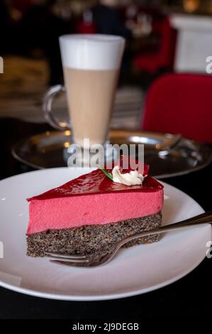 Pezzo di famosa torta di semi di papavero con mousse di lamponi di origine austriaca servito con panna montata e una tazza di caffè latte in vecchio classico caffè-ristorante Foto Stock