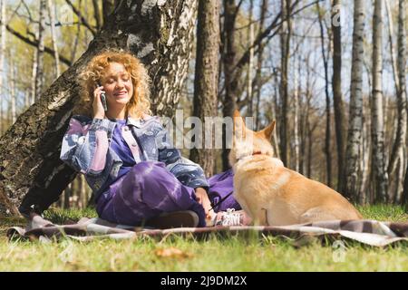 ragazza su un pic-nic con il suo cane durante la giornata calda di sole nel parco, ragazza che parla con il suo telefono cellulare all'aperto. Foto di alta qualità Foto Stock