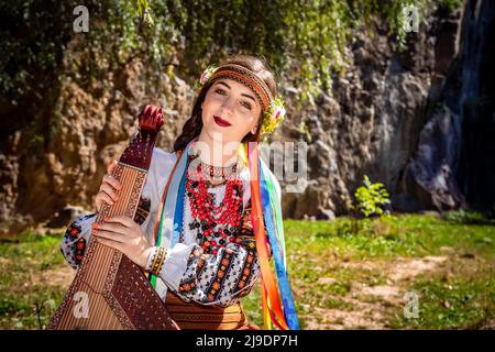 Il musicista ucraino in autentico vestito nazionale siede su una roccia. Donna Ucraina con uno strumento musicale bandura prima di eseguire musica folk Foto Stock