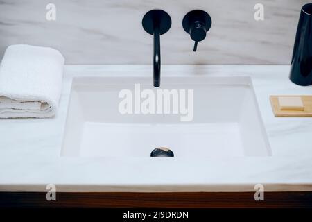 Lavandino con elegante rubinetto nero, sapone e asciugamano. Lavandino con ripiano in marmo in bagno Foto Stock