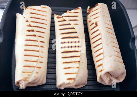 Shawarma o kebab confezionate con carne e verdure alla griglia e confezionate in pane piatto. Avvolgete la grigliatura sul grill. Foto Stock