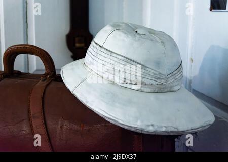 Cappello Vintage Safari e valigia in pelle contro la parete bianca. Foto Stock