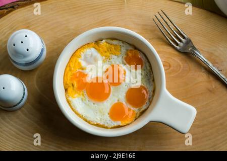 Uova di quaglia fritte in tegame di uovo di ceramica, su superficie di legno, vista dall'alto Foto Stock