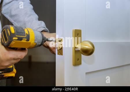 La mano del fabbro tiene il cacciavite nell'installazione della nuova serratura della porta della casa Foto Stock