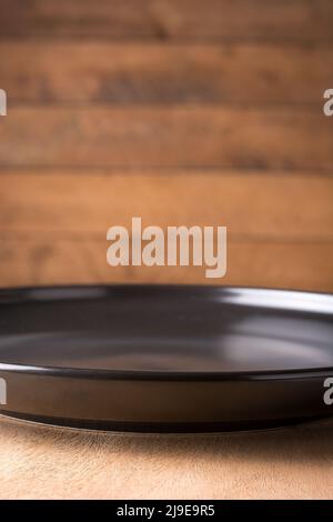lastra nera vuota su un tavolo in legno contro sfondo di legno sfocato, sfondo fotografico alimentare o sfondo, primo piano vista laterale Foto Stock