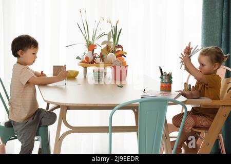 Bambini divertirsi a casa al tavolo, creare arte fatta a mano. Bambini disegnare e comunicare in cucina, intelletto emotivo Foto Stock