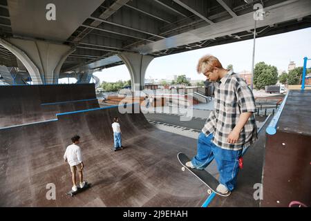 Ritratto ad angolo alto del ragazzo adolescente in piedi sulla rampa allo skatepark e fare skateboard trucchi, copia spazio Foto Stock