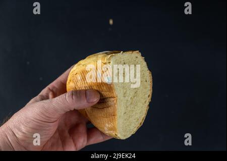 Un uomo tiene un pezzo di pane ammuffito su uno sfondo nero. Mano di un uomo cresciuto con un pezzetto di pane di grano stantio. Foto Stock