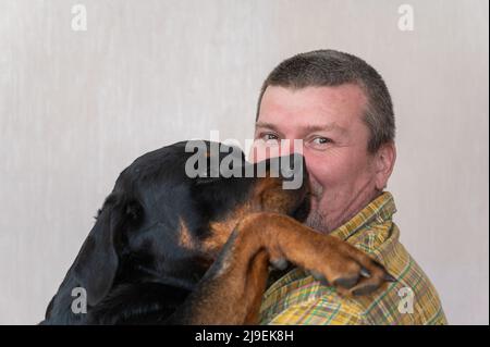 Ritratto di un uomo felice cresciuto coccolare il suo grande cane nero. Uomo con taglio corto e capelli graffati. Una femmina Rottweiler cane mette la sua zampa sulla spalla Foto Stock