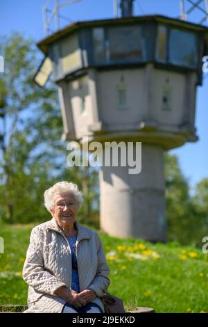 PRODUZIONE - 09 maggio 2022, Sassonia-Anhalt, Hötensleben: Testimone contemporaneo Gitta Kappe siede al 'Monumento al confine Hötensleben' di fronte ad una ex torre di guardia. Il confine è stato chiuso proprio come Gitta Kappe era sul lato sbagliato per lei. Il 26 maggio 1952, l'allora 20 anni era al lavoro a Schöningen nella FRG; come bambina e cameriera, era il buon spirito nella famiglia di un medico. Ha sempre percorso la sua bicicletta per i quattro chilometri alla sua città natale di Hötensleben, l'ormai 90 anni ricorda. A casa, quella era i suoi genitori e la sua fidanzata. Foto: Klaus-Dietmar Gabbert/dpa Foto Stock