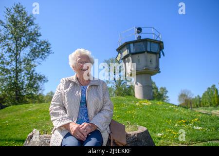 PRODUZIONE - 09 maggio 2022, Sassonia-Anhalt, Hötensleben: Testimone contemporaneo Gitta Kappe siede al 'Monumento al confine Hötensleben' di fronte ad una ex torre di guardia. Il confine è stato chiuso proprio come Gitta Kappe era sul lato sbagliato per lei. Il 26 maggio 1952, l'allora 20 anni era al lavoro a Schöningen nella FRG; come bambina e cameriera, era il buon spirito nella famiglia di un medico. Ha sempre percorso la sua bicicletta per i quattro chilometri alla sua città natale di Hötensleben, l'ormai 90 anni ricorda. A casa, quella era i suoi genitori e la sua fidanzata. Foto: Klaus-Dietmar Gabbert/dpa Foto Stock