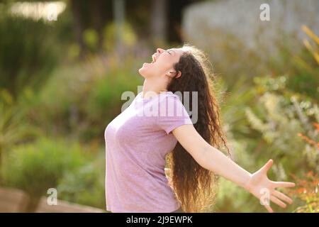 Ritratto laterale di una donna eccitata che stretching braccia e urla in un parco Foto Stock