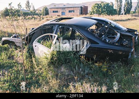 Discarica di auto, rottami di metallo. Primo piano di una vecchia auto abbandonata in un cortile con erba che germogliano all'interno e ciottoli troppo coltivati. Il sole si riflette Foto Stock