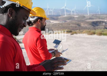 Uomini ingegnere multirazziale che lavorano alla fattoria mulino a vento con tablet e drone digitale - Focus sul volto africano uomo Foto Stock