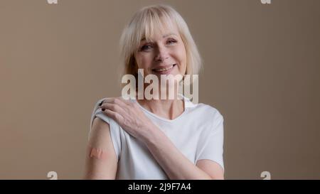 Coronavirus immunizzazione infezione covid19 vaccinazione felice vaccinato anziana donna matura posando con adesivo cerotto medico sul braccio dopo Foto Stock