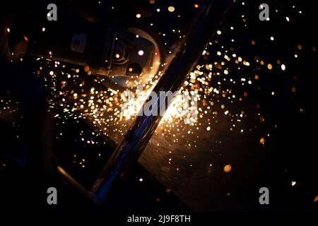 Scintille da metallo di macinazione. Lavorazione dell'acciaio in officina. Si illumina al buio. Produzione di pezzi. Il taglio è diventato smerigliatrice. Lavorazione dei cordoni di saldatura. Foto Stock