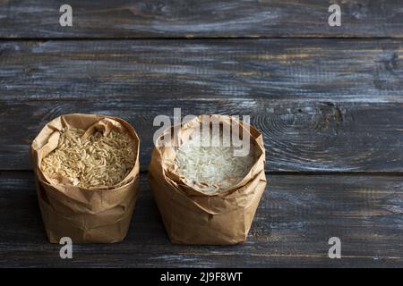 Riso basmati crudo a grana lunga marrone e bianco in sacchetti di carta artigianale su sfondo di legno, spazio Foto Stock