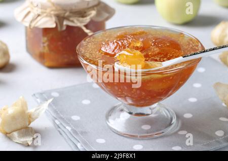 Marmellata fatta in casa physalis trasparente e mele in ciotola e vaso di vetro su sfondo grigio Foto Stock