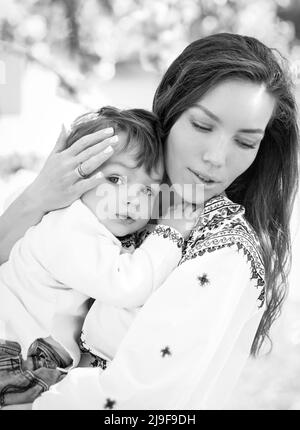 Foto in bianco e nero piccolo bambino sulle mani della madre. Ritratto di famiglia di due persone. Primavera paesaggio sfondo. Foto Stock