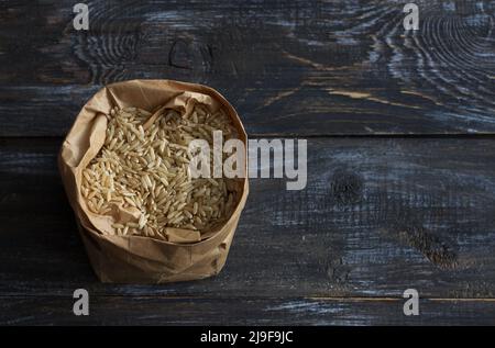 Riso bruno crudo a grana lunga in un sacco di carta artigianale su uno sfondo di legno, spazio Foto Stock