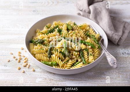 Pasta vegana con asparagi, aglio, pinoli e prezzemolo su sfondo ligneo. Semplice cibo fatto in casa Foto Stock