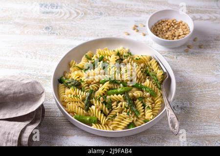 Pasta vegana con asparagi, aglio, pinoli e prezzemolo su sfondo di legno, vista dall'alto. Semplice cibo fatto in casa Foto Stock