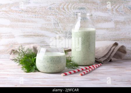 Sano verde kefir dietetico (yogurt) con erbe in vetro e bottiglia su tavola di legno Foto Stock