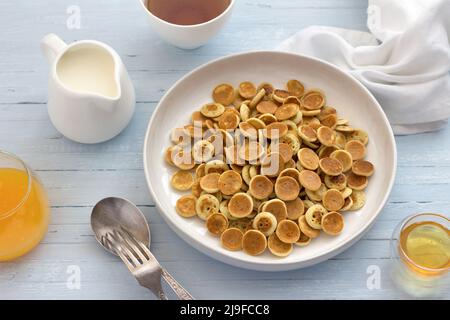 Piatto di cereali Mini Pancakes con miele, crema e succo d'arancia fresco su sfondo azzurro. Cibo alla moda. Colazione fatta in casa. Vista dall'alto Foto Stock