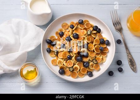 Piatto di mini pancake cereali con miele, bacche, panna e succo d'arancia fresco su sfondo azzurro. Cibo alla moda. Colazione fatta in casa. Vista dall'alto Foto Stock