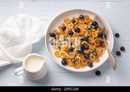 Piatto di mini pancake con cereali con crema, miele e frutti di bosco su sfondo blu chiaro. Cibo alla moda. Colazione fatta in casa. Vista dall'alto Foto Stock